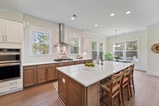 4235 Royal Harbor Rd, Hollywood, SC 29449 - kitchen with tasteful backsplash, wall chimney range hood, appliances with stainless steel finishes, brown cabinets, and wood finished floors