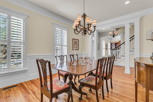 dining space featuring visible vents, a notable chandelier, light wood-style flooring, crown molding, and stairs