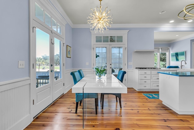 dining area featuring french doors, light wood-style floors, wainscoting, crown molding, and a chandelier