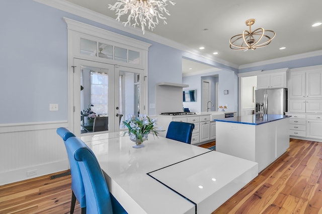 dining room featuring light wood-style flooring, ornamental molding, a wainscoted wall, and a chandelier