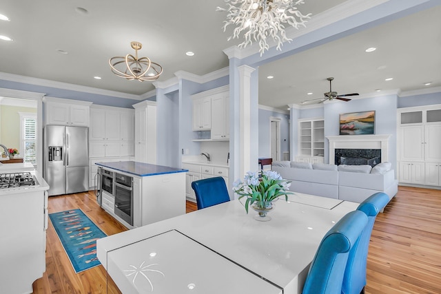 dining area featuring light wood-style floors, ornamental molding, a high end fireplace, and ceiling fan with notable chandelier