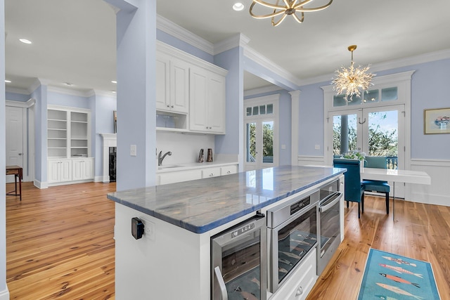 kitchen with beverage cooler, ornamental molding, white cabinets, light wood-type flooring, and a chandelier