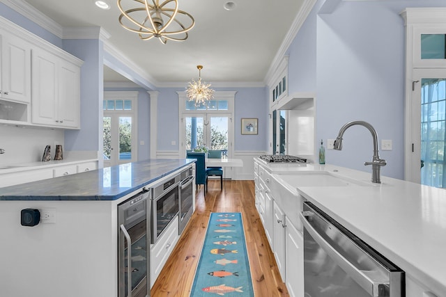 kitchen with ornamental molding, wine cooler, appliances with stainless steel finishes, white cabinets, and a chandelier