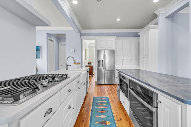 kitchen with white cabinets, stainless steel appliances, light wood-style floors, and ornamental molding