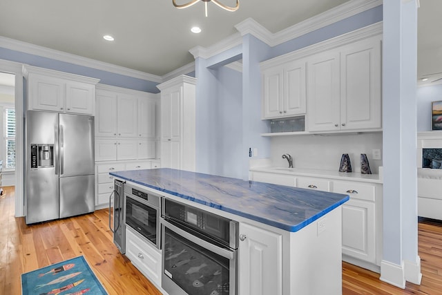 kitchen with white cabinets, light wood-type flooring, appliances with stainless steel finishes, and a kitchen island