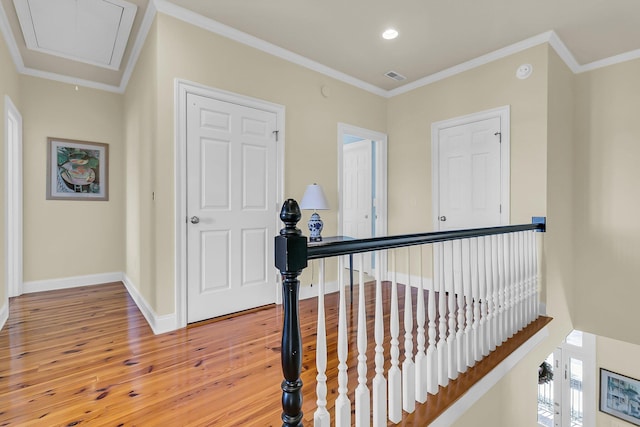 hall with visible vents, an upstairs landing, light wood-style flooring, crown molding, and attic access