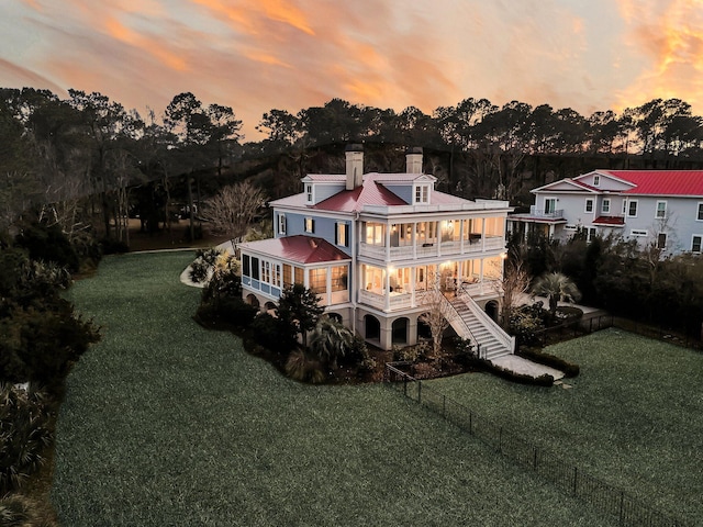 back of house with stairs, a lawn, a chimney, a balcony, and a fenced backyard