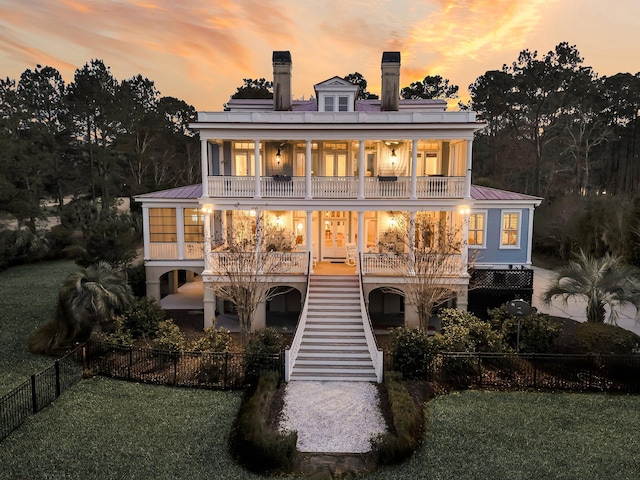 back of house at dusk with fence, stairway, metal roof, a balcony, and a patio area