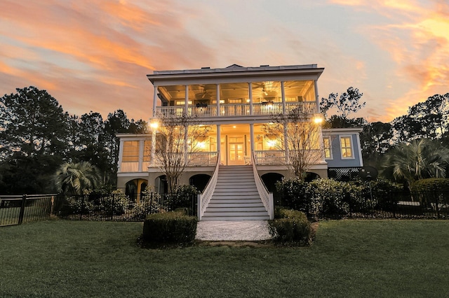 back of property at dusk featuring a balcony, fence, a yard, ceiling fan, and stairs