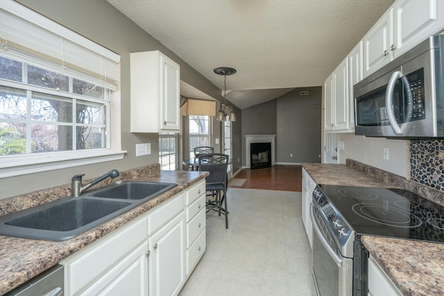 kitchen featuring white cabinets, appliances with stainless steel finishes, vaulted ceiling, a fireplace, and a sink