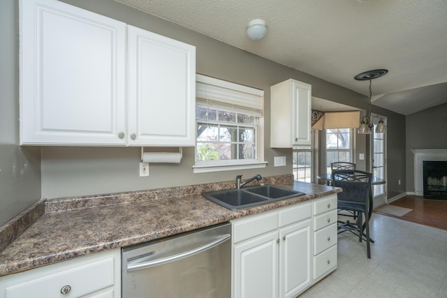 kitchen featuring white cabinets, dark countertops, a fireplace with flush hearth, stainless steel dishwasher, and a sink