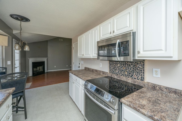 kitchen with appliances with stainless steel finishes, open floor plan, hanging light fixtures, a fireplace, and white cabinetry