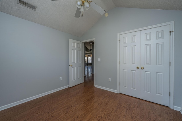 unfurnished bedroom featuring baseboards, visible vents, lofted ceiling, wood finished floors, and a closet