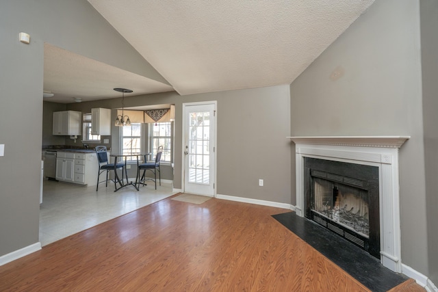 unfurnished living room featuring baseboards, a fireplace with flush hearth, wood finished floors, vaulted ceiling, and a textured ceiling