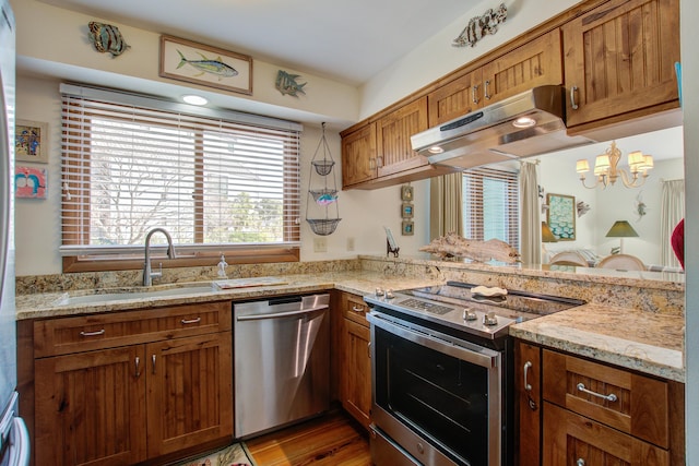 kitchen featuring appliances with stainless steel finishes, brown cabinets, a sink, and under cabinet range hood