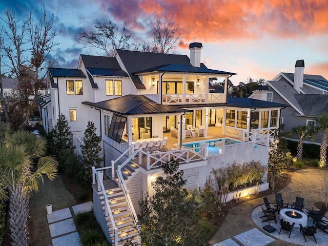 back house at dusk featuring an outdoor living space with a fire pit, a patio area, a sunroom, and a balcony