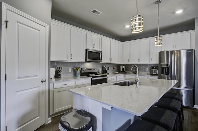 kitchen featuring pendant lighting, sink, light stone countertops, an island with sink, and appliances with stainless steel finishes