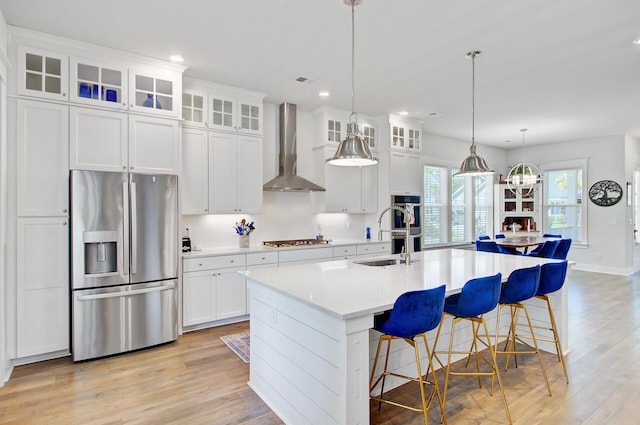 2557 Hatch Dr, Johns Island, SC 29455 - kitchen with wall chimney range hood, appliances with stainless steel finishes, a sink, light wood finished floors, and an island with sink