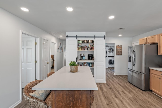 kitchen featuring stacked washer / dryer, stainless steel fridge with ice dispenser, a center island, and a barn door