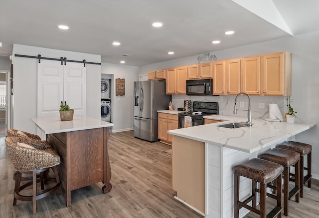 kitchen with stacked washer and dryer, a barn door, kitchen peninsula, a kitchen breakfast bar, and black appliances