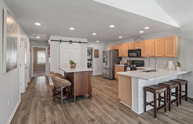 kitchen with a barn door, black appliances, a breakfast bar, sink, and stacked washer and clothes dryer