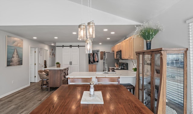 dining room with a barn door, vaulted ceiling, and dark hardwood / wood-style floors