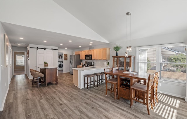 dining space with high vaulted ceiling, stacked washing maching and dryer, a barn door, and light wood-type flooring