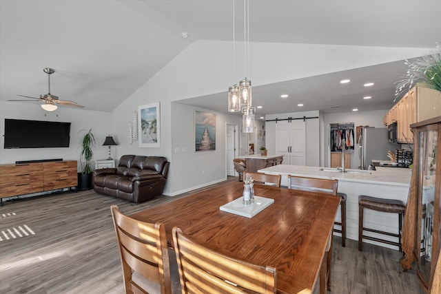 dining space with lofted ceiling, a barn door, ceiling fan, sink, and hardwood / wood-style flooring