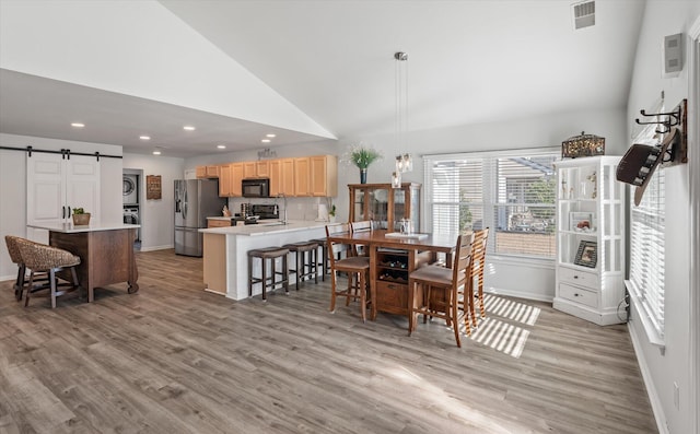 dining room with high vaulted ceiling, a barn door, stacked washer and dryer, and light hardwood / wood-style flooring