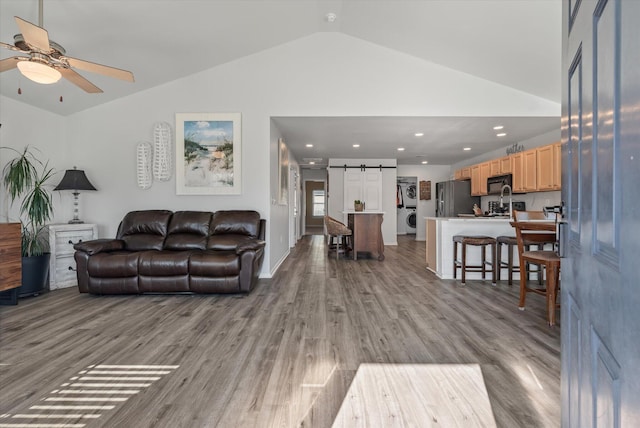 living room with a barn door, ceiling fan, light wood-type flooring, lofted ceiling, and stacked washer / dryer