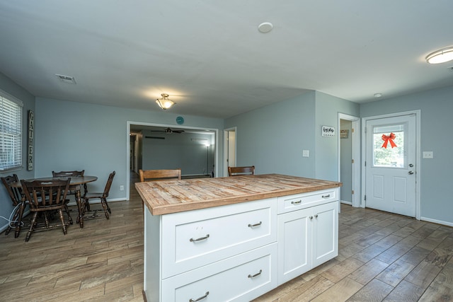 kitchen featuring butcher block countertops, a center island, light wood-type flooring, and white cabinets