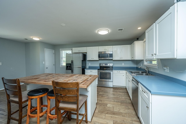 kitchen featuring white cabinets, appliances with stainless steel finishes, a breakfast bar, wood counters, and sink