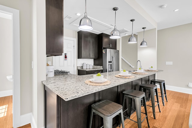 kitchen with high end fridge, light stone countertops, pendant lighting, light hardwood / wood-style flooring, and a breakfast bar