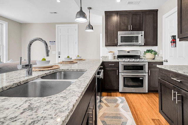 kitchen with light hardwood / wood-style flooring, stainless steel appliances, decorative light fixtures, light stone counters, and sink