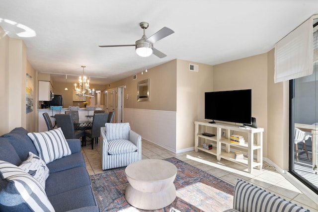 living room featuring light tile patterned flooring, visible vents, ceiling fan with notable chandelier, and wainscoting