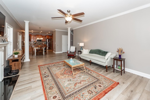 living room featuring light wood-type flooring, ornamental molding, a ceiling fan, baseboards, and ornate columns