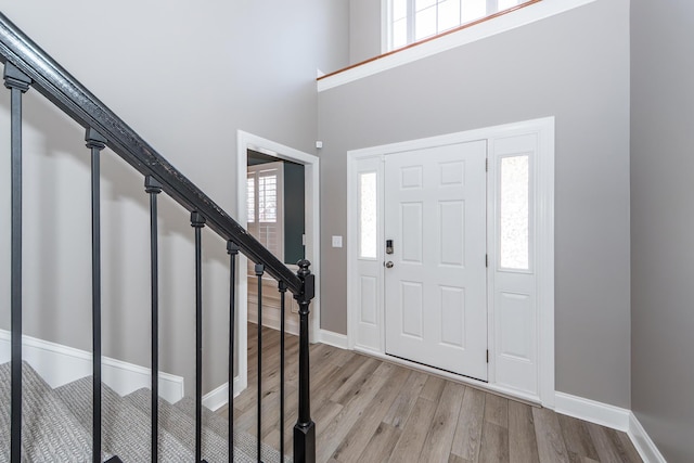 foyer entrance featuring light wood-type flooring, baseboards, a towering ceiling, and stairway