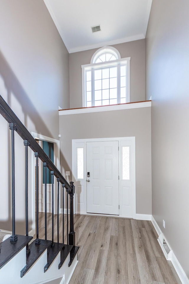 foyer entrance featuring wood finished floors, visible vents, baseboards, a towering ceiling, and crown molding