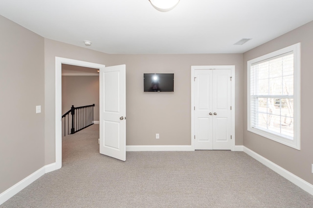 unfurnished bedroom featuring baseboards, light carpet, a closet, and visible vents