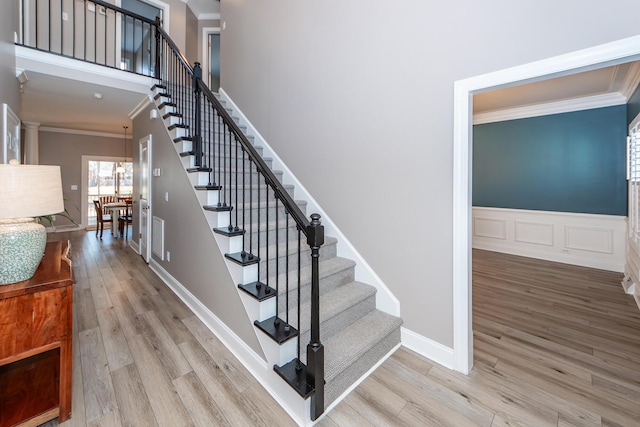 stairway with wood finished floors, a wainscoted wall, visible vents, a towering ceiling, and crown molding