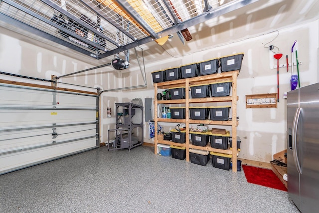 garage featuring electric panel, baseboards, a garage door opener, and stainless steel refrigerator with ice dispenser