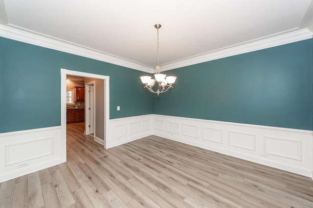 unfurnished room featuring a wainscoted wall, an inviting chandelier, crown molding, and light wood-type flooring