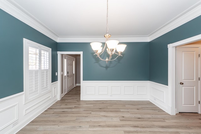 unfurnished dining area featuring a notable chandelier, ornamental molding, light wood-type flooring, and a wainscoted wall