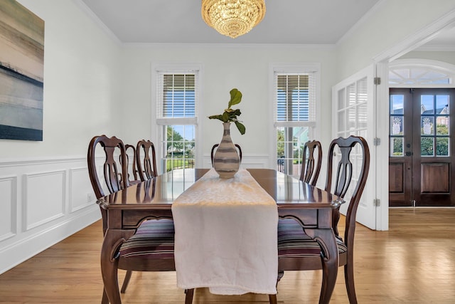 dining space featuring a chandelier, french doors, light wood-style flooring, ornamental molding, and wainscoting