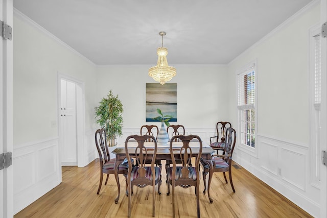 dining space featuring light wood-type flooring, ornamental molding, wainscoting, a chandelier, and a decorative wall