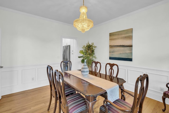 dining space featuring a chandelier, crown molding, a wainscoted wall, light wood-style floors, and a decorative wall