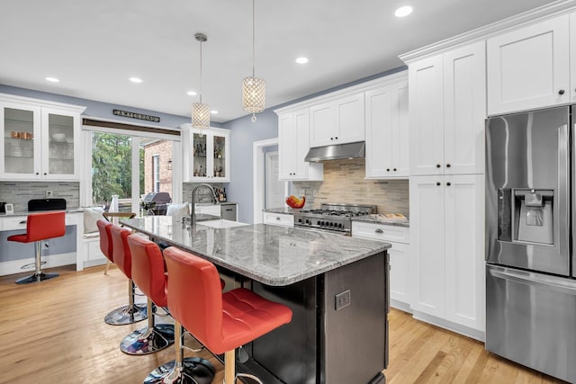kitchen featuring appliances with stainless steel finishes, decorative backsplash, a sink, light wood-type flooring, and glass insert cabinets