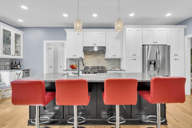 kitchen featuring stainless steel fridge, under cabinet range hood, backsplash, white cabinets, and recessed lighting