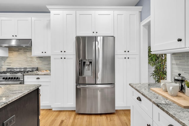 kitchen with appliances with stainless steel finishes, under cabinet range hood, white cabinetry, tasteful backsplash, and light wood finished floors