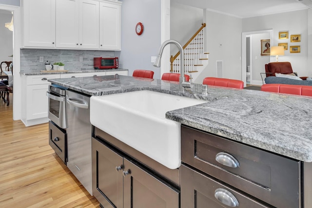 kitchen featuring a sink, light wood finished floors, decorative backsplash, white cabinets, and crown molding